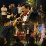 Magician in a red bow tie performing a magic trick for a child at an outdoor evening birthday party